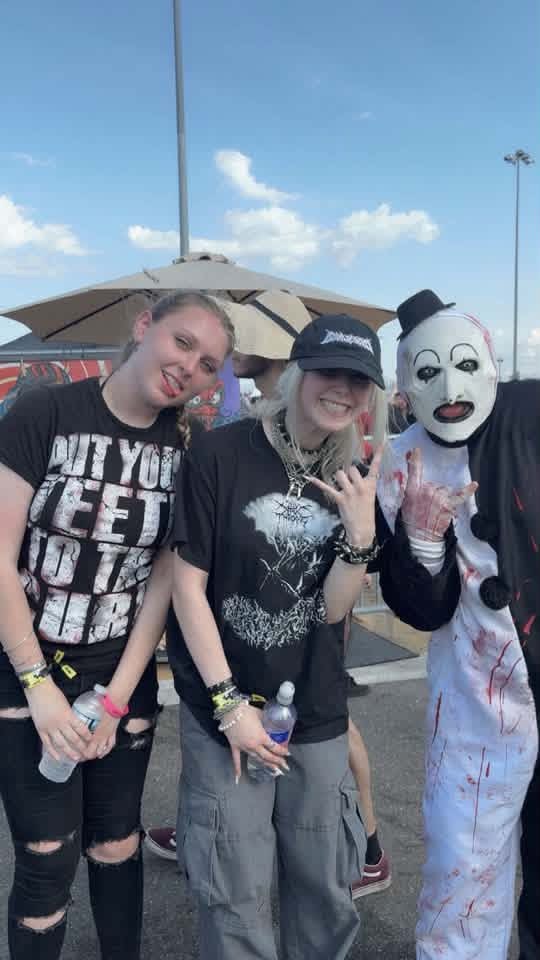 Art the Clown throwing horns with two fans in the sunny parking lot