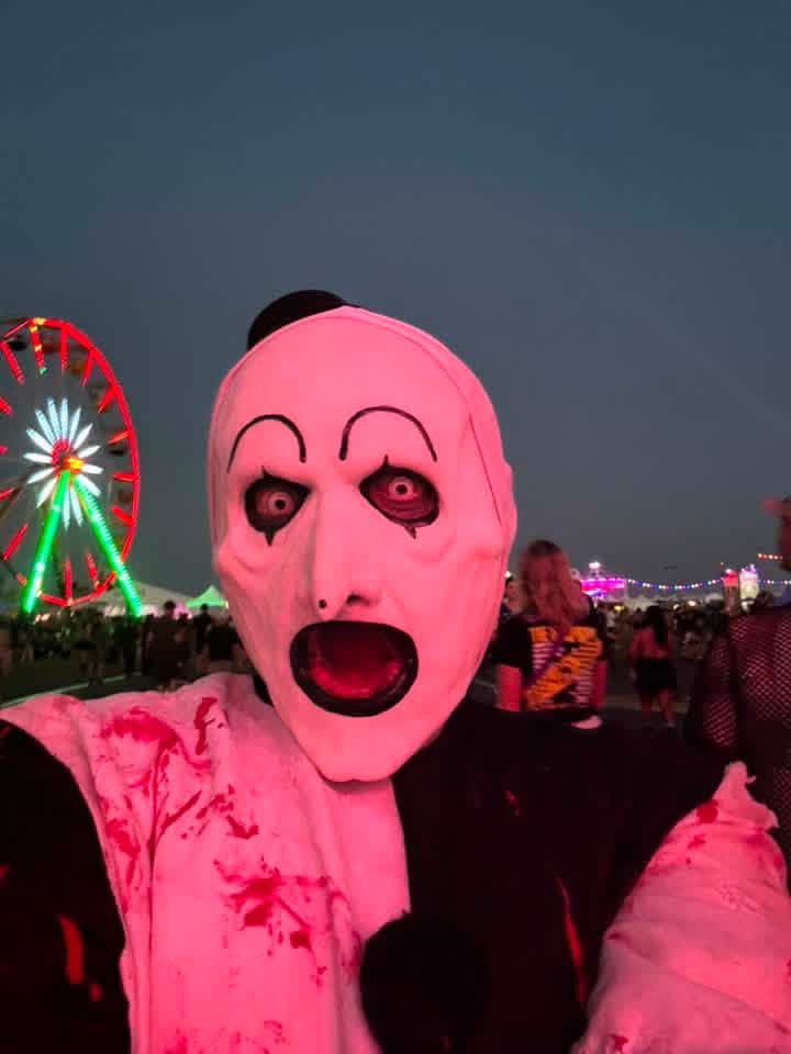 Art the Clown screaming into the camera at dusk with the ferris wheel behind him