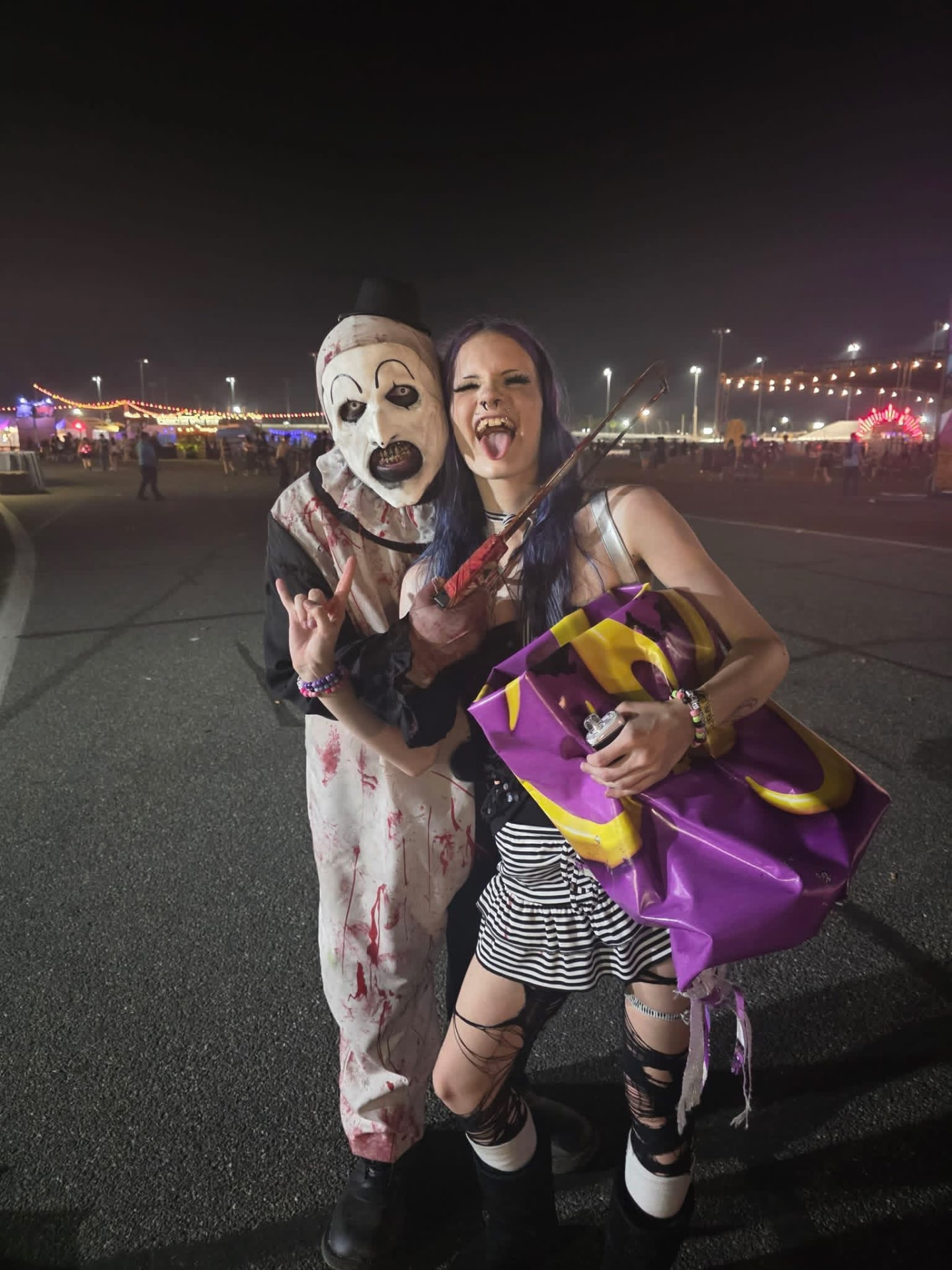 Art the Clown throwing horns with a fan with purple hair in the parking lot at night