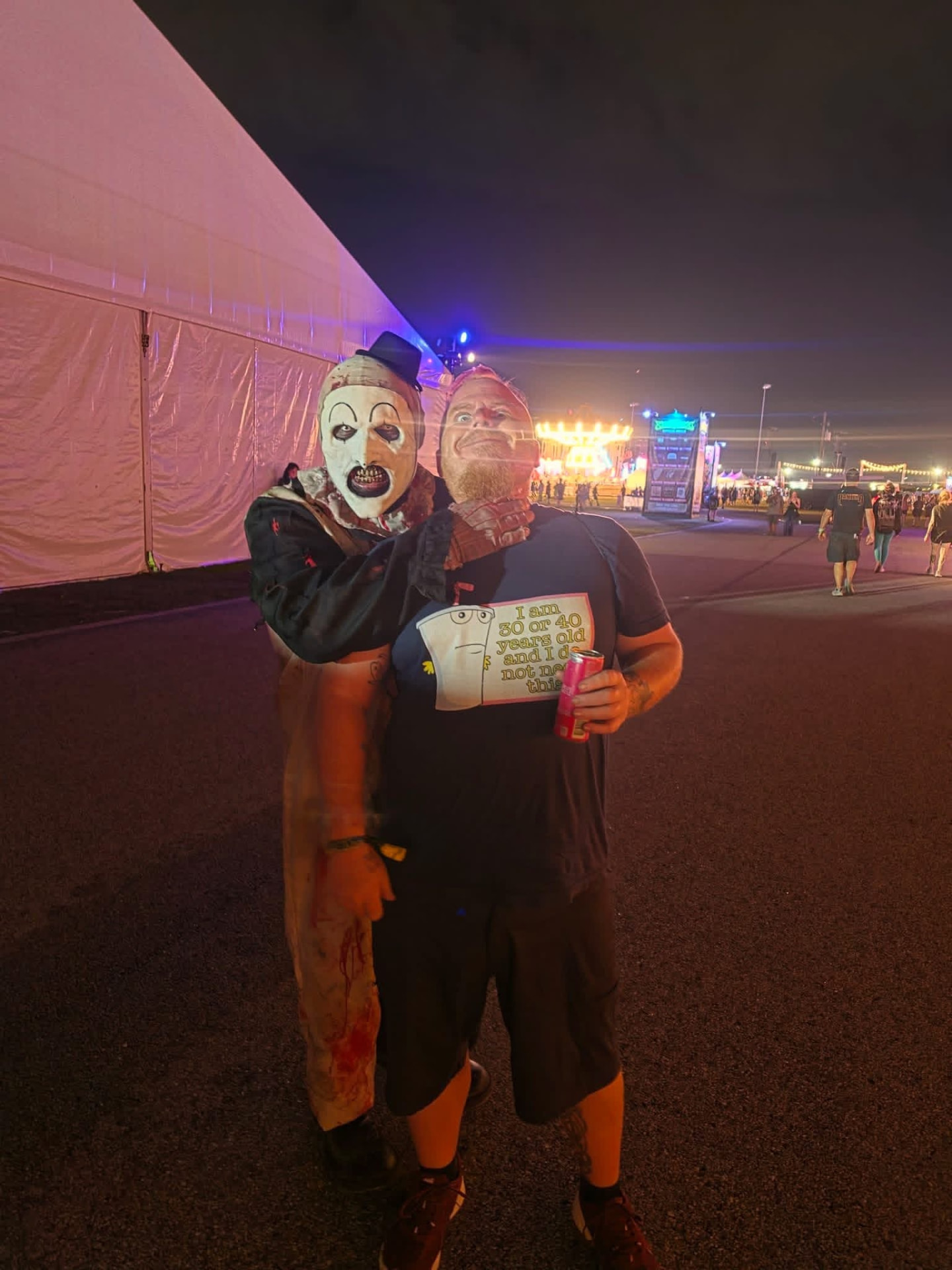 Art the Clown hanging off a fan's shoulder at night by the big tent
