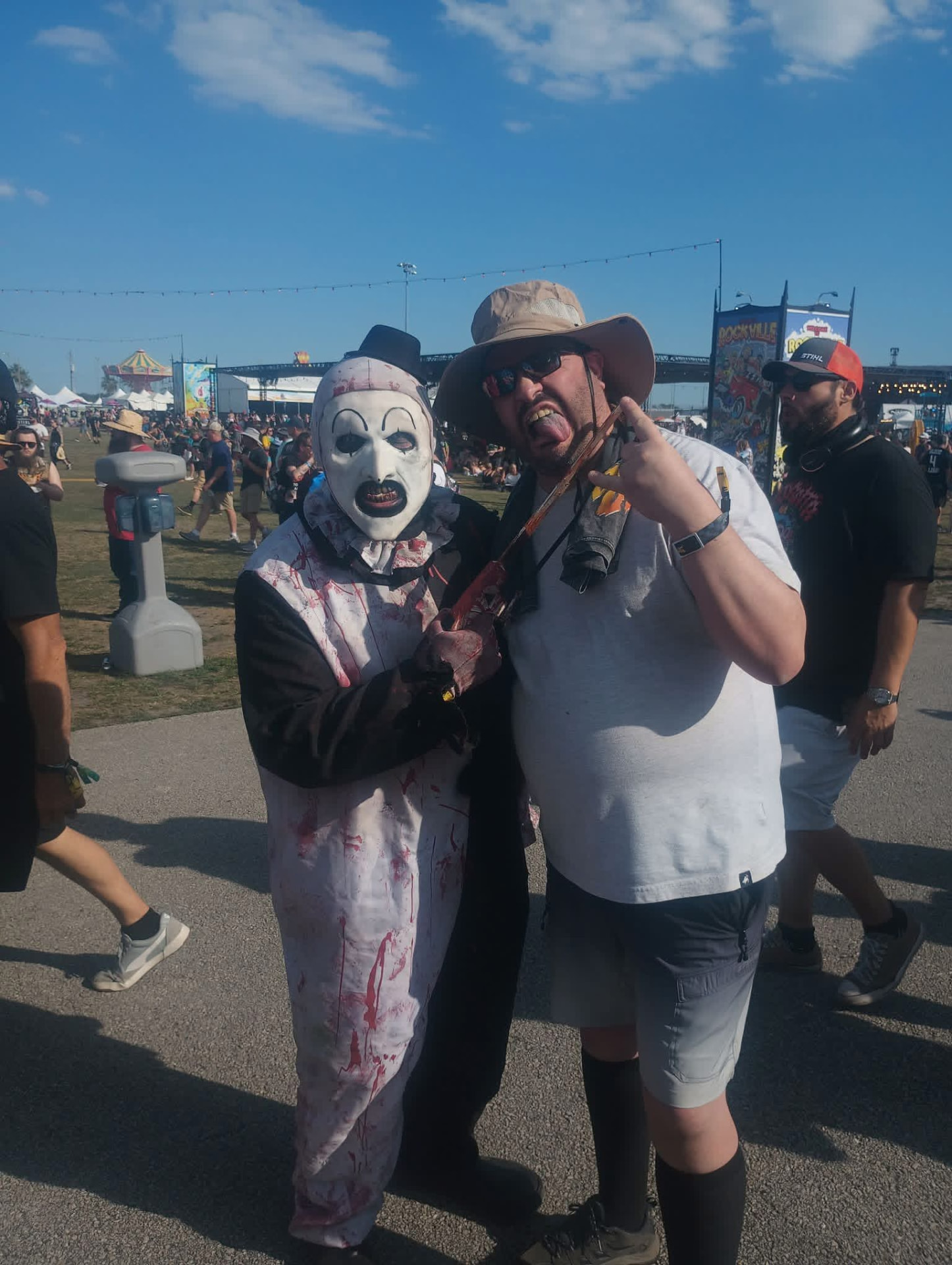 Art the Clown with a bloody blade next to a laughing fan in a bucket hat at Rockville