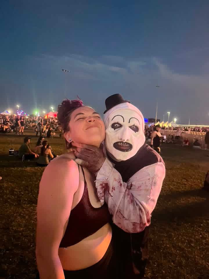 Art the Clown with his gloved hand on a laughing fan's throat at blue hour