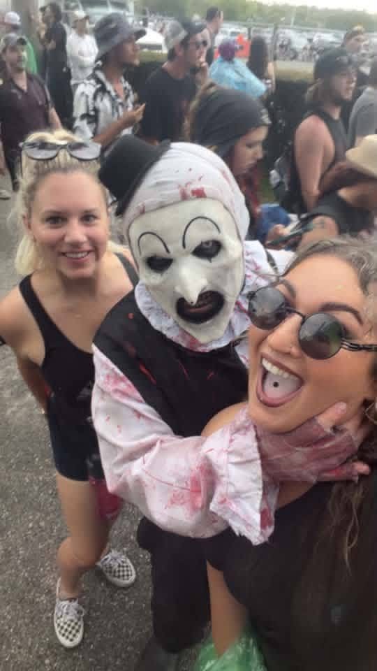 Group selfie: Art the Clown between two grinning fans in the festival crowd