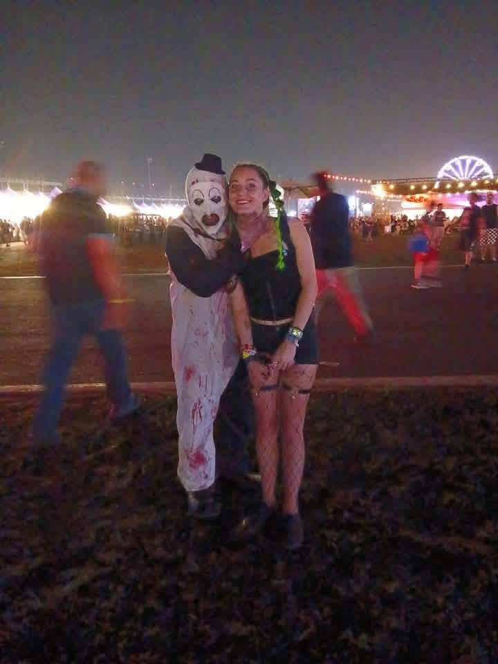 Art the Clown hugging a fan with green braids under the ferris wheel at night