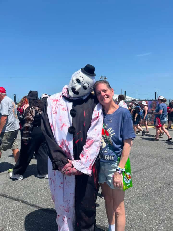 Art the Clown posing with a fan in the sunny festival parking lot
