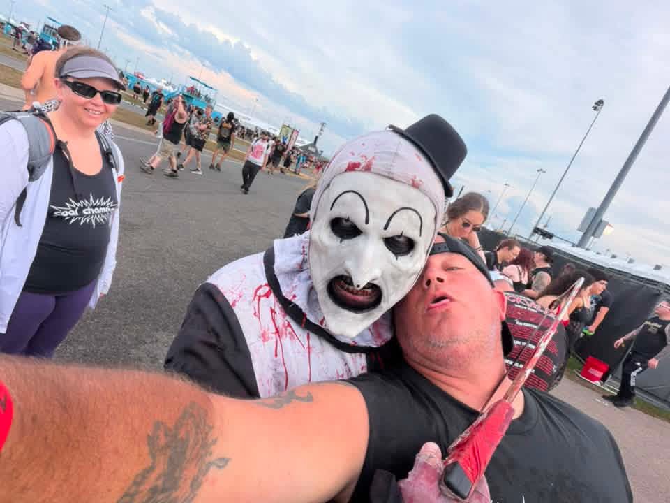 Art the Clown with a bloody blade leaning into a fan's selfie in the parking lot