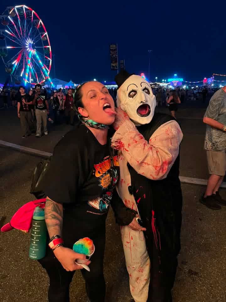 Art the Clown grabbing a fan's throat in front of the lit ferris wheel at night