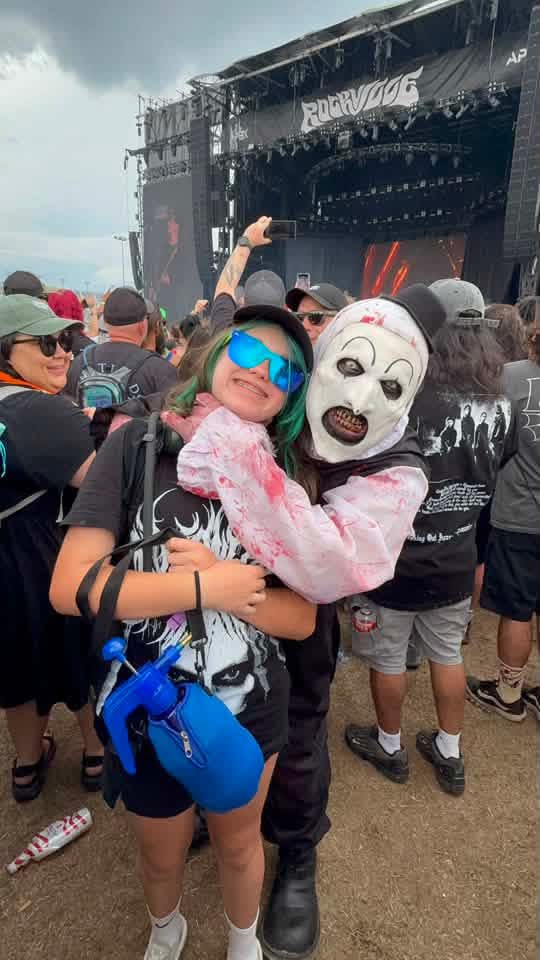 Art the Clown hugging a fan in blue shades in front of the Rockville main stage