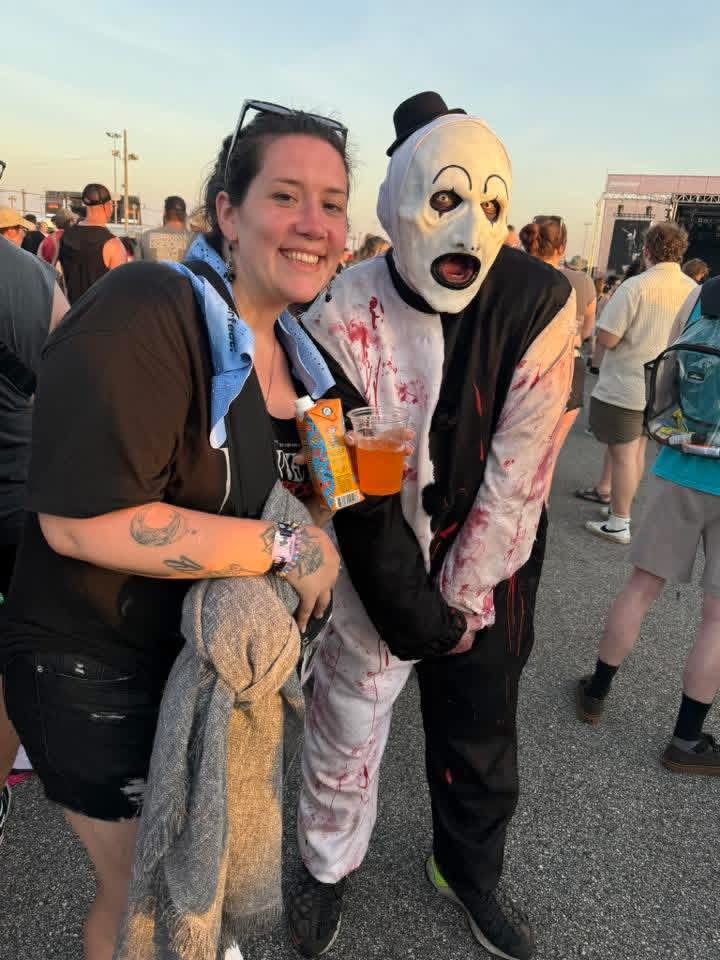 Sunset: Art the Clown holding a drink and posing with a smiling fan