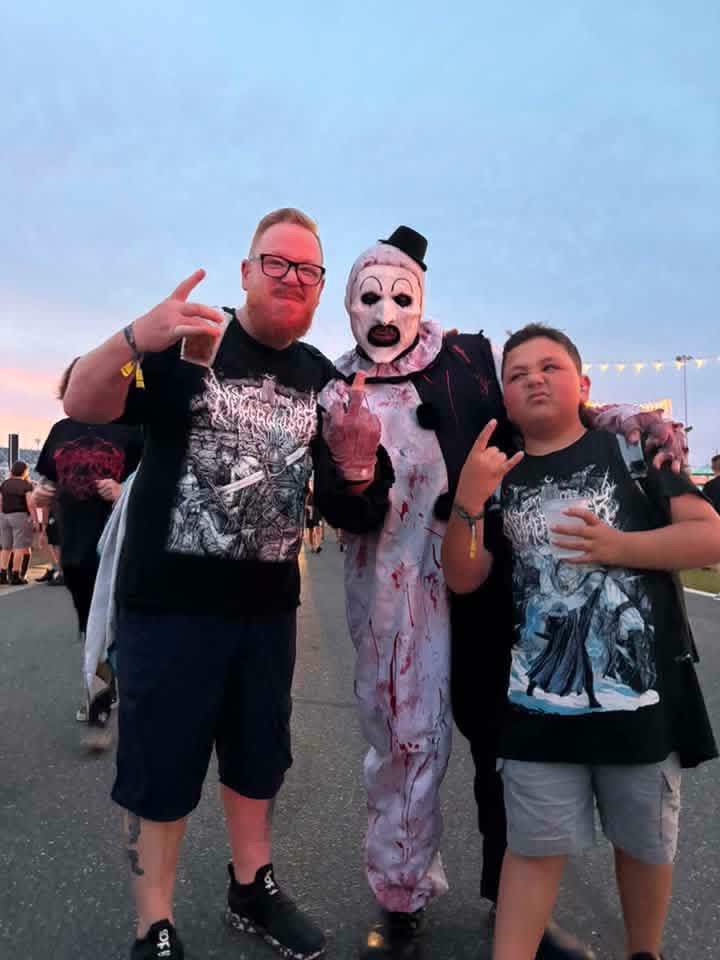 Art the Clown between a dad and his son, all throwing horns at dusk