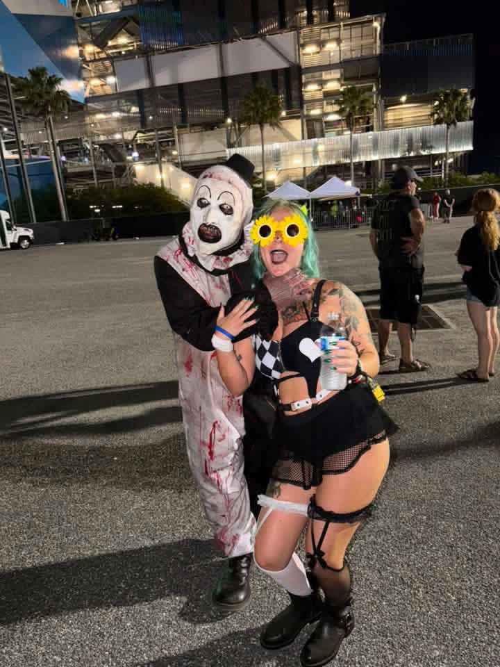 Night parking lot: Art the Clown posing with a fan in sunflower glasses outside the stadium