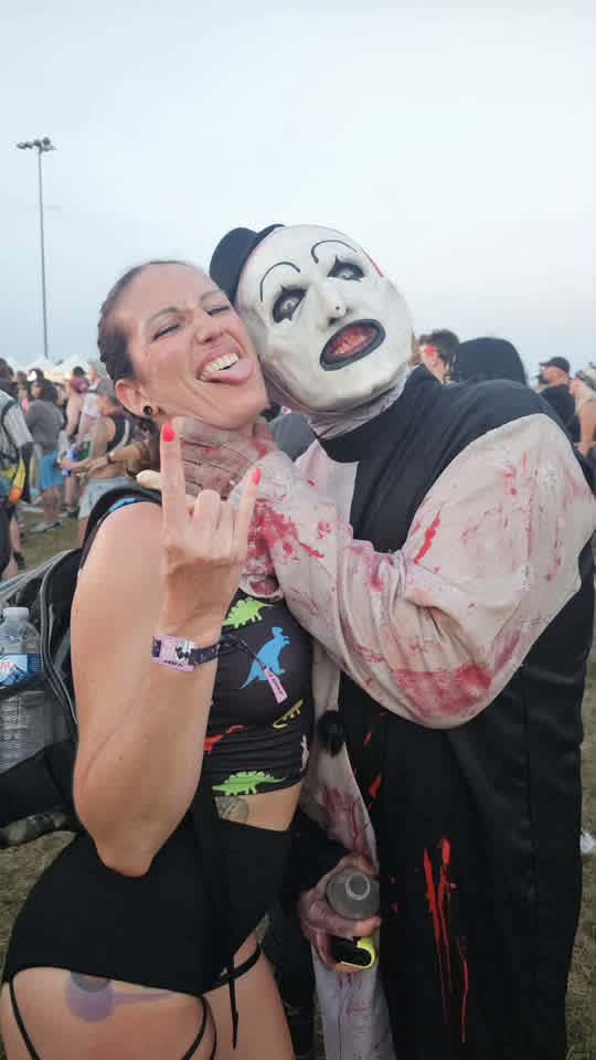 Art the Clown cheek to cheek with a fan throwing horns on the field