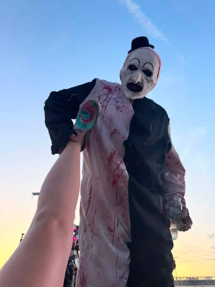 Low-angle shot of Art the Clown handing a fan a drink at sunset