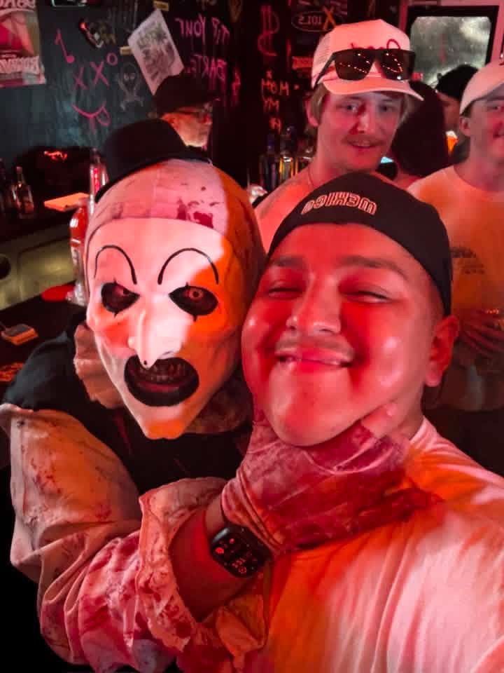 Red-lit bar selfie: Art the Clown with a fan in a backwards cap