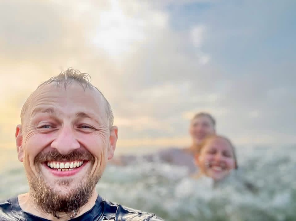 Aleksandr out of costume, laughing in the ocean with his family behind him